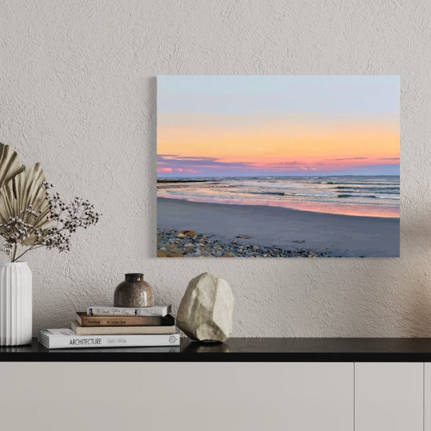 Canvas print of a beach scene with a sunset hanging on a wall above a shelf.