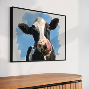 Framed artwork of a cow's face on a wall above a wooden cabinet.